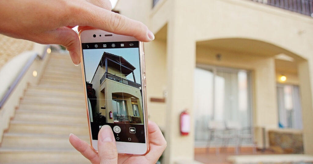 woman taking a cell phone picture of the outside of a house